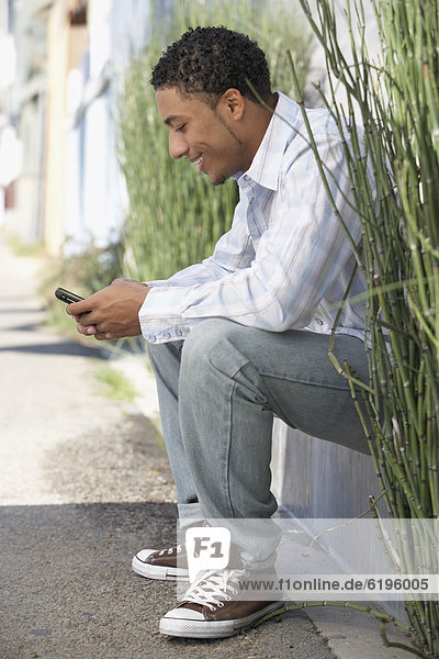 Young mixed race man sitting outdoors with cell phone
