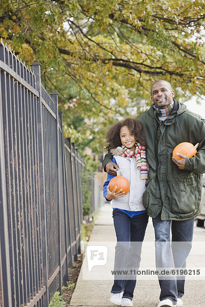 African father and daughter walking with pumpkins