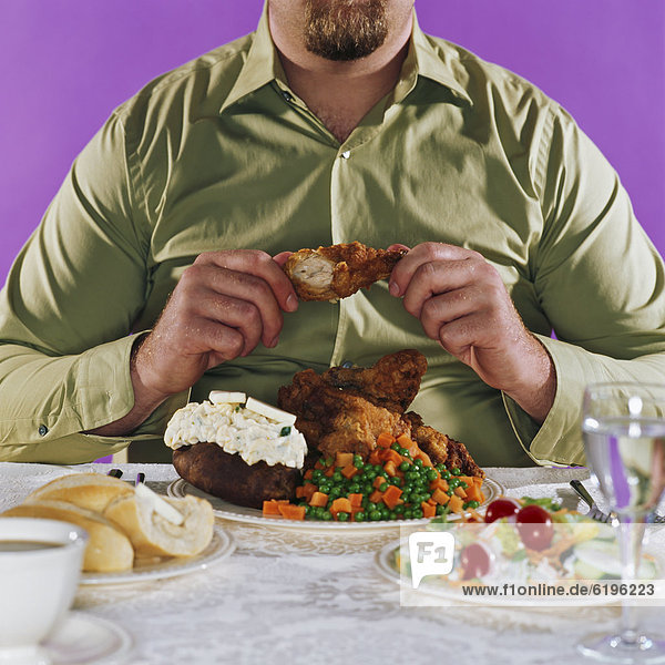 Overweight man eating fried chicken dinner