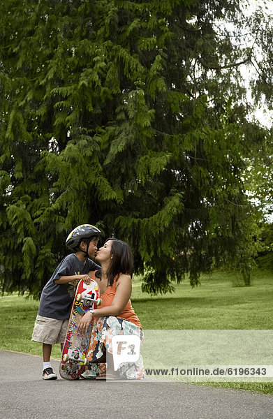 Asian boy with skateboard kissing mother