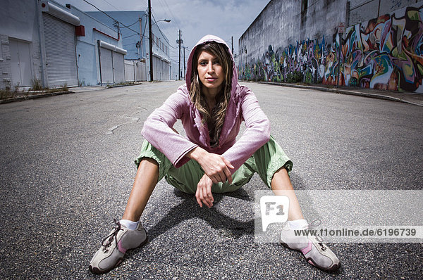 Hispanic woman sitting in alley with graffiti
