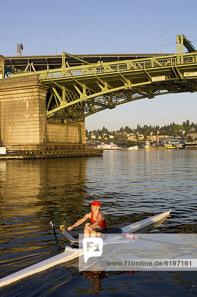 Person rowing sculling boat on river under bridge