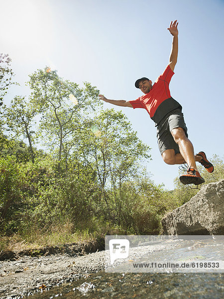 Mixed race man jumping into stream