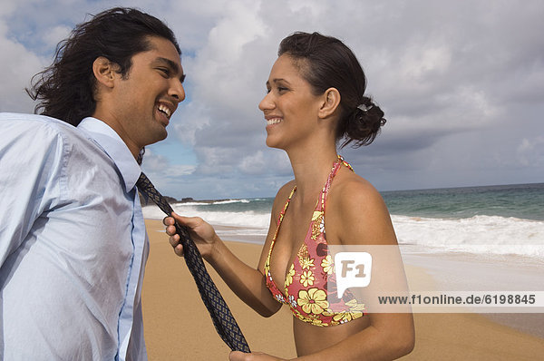 Woman pulling man's necktie at beach