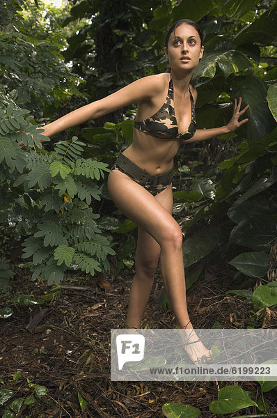 Hispanic woman wearing camouflage bikini in jungle