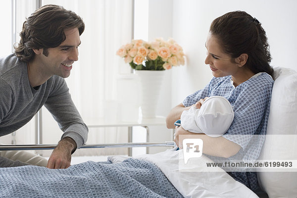 Hispanic couple holding newborn baby in hospital bed