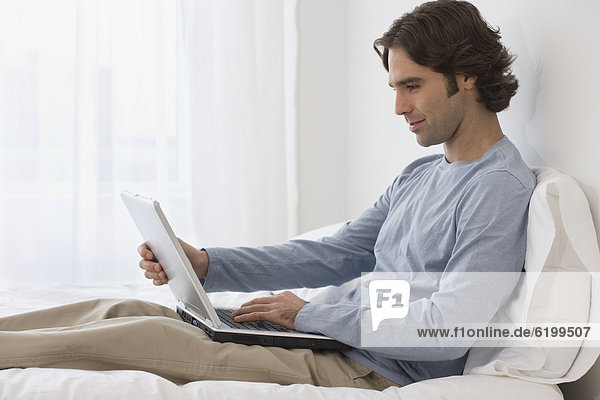 Hispanic man using laptop on bed