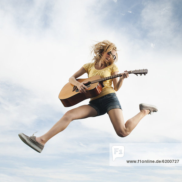 Caucasian woman jumping in mid-air playing guitar