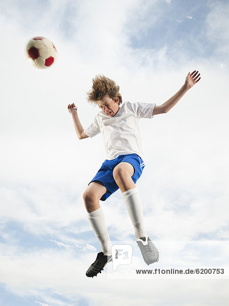 Caucasian teenager heading soccer ball in mid-air