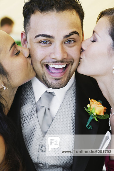 Groom being kissing by two women
