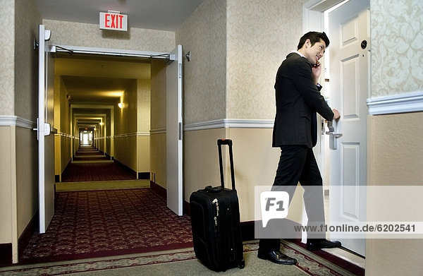 Asian businessman using cell phone and entering hotel room