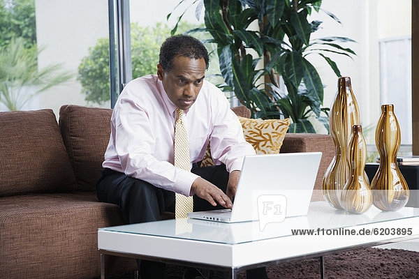 Serious African businessman typing on laptop in living room