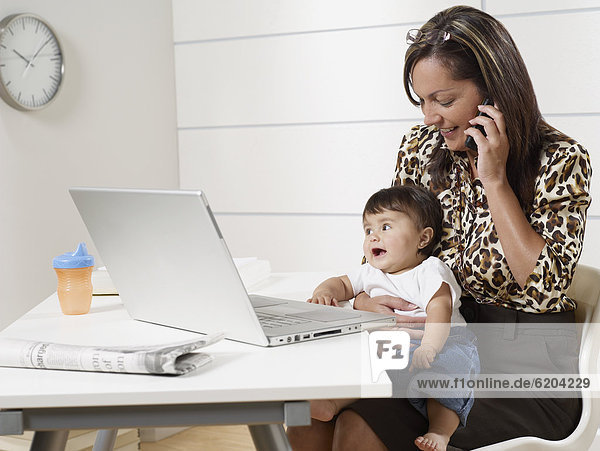 Hispanic working mother holding baby son and talking on phone