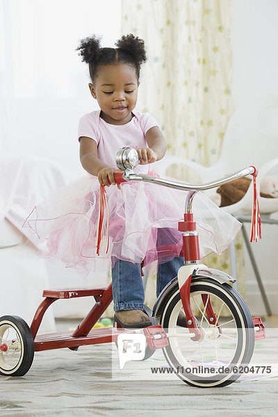 African American girl in costume riding tricycle