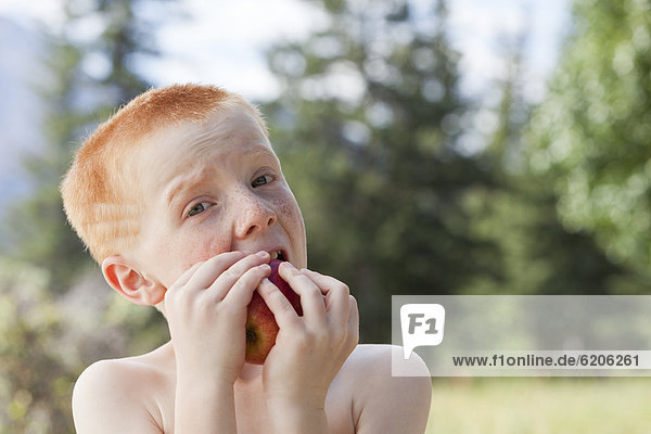 Freckled boy eating an apple outdoors