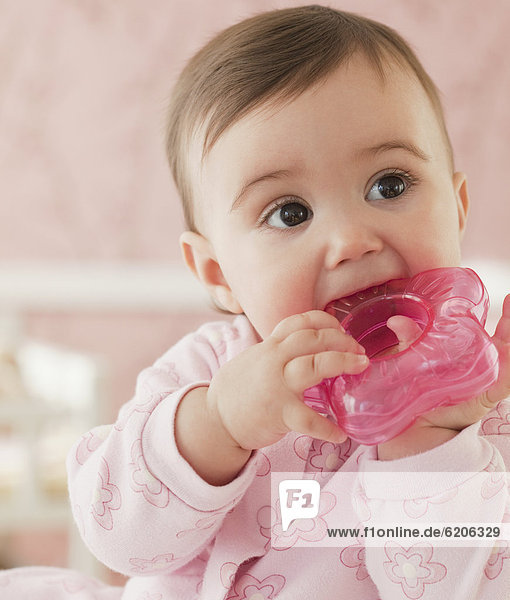 Mixed race baby girl chewing on plastic toy