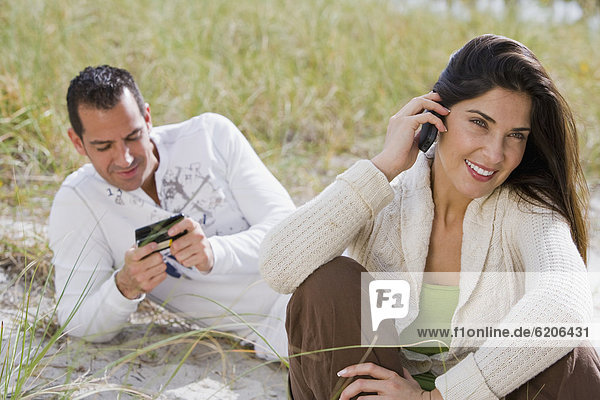 Hispanic couple talking on cell phones at beach