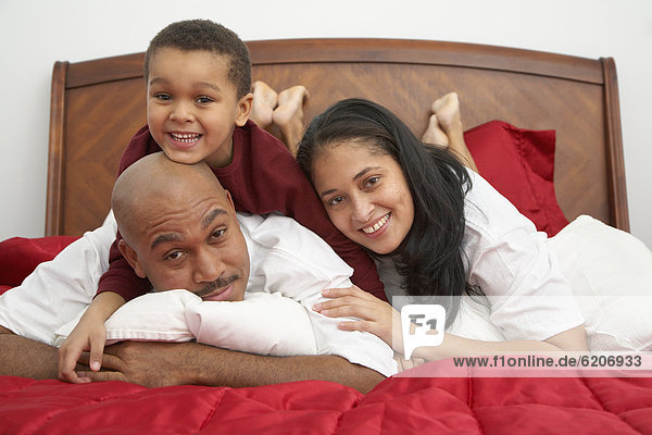 Mixed race boy lounging on bed with parents