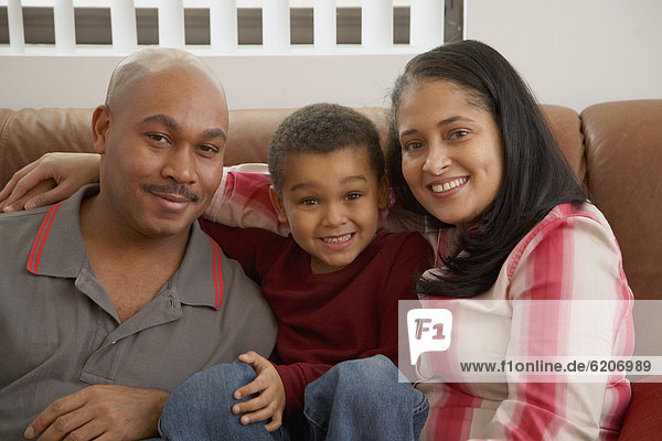 Mixed race boy snuggling on couch with parents