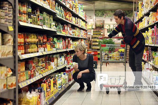 Junges Paar beim Einkauf zwischen Regalen mit diversen Lebensmitteln  Lebensmittelabteilung  Supermarkt  Deutschland  Europa