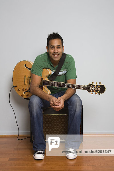Mixed race man sitting with electric guitar