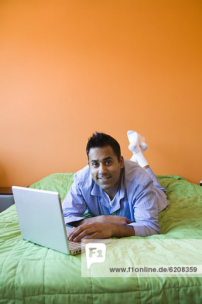 Mixed race man using laptop on bed