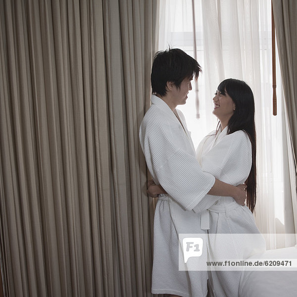 Asian couple in bathrobes hugging in hotel room