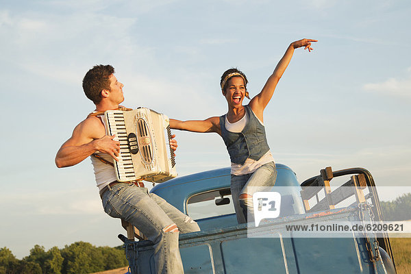 Man playing accordion for girlfriend in back of truck