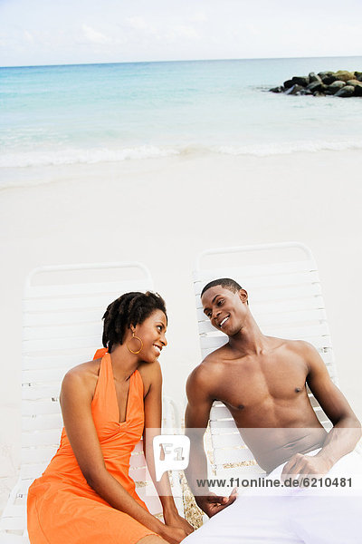 African couple sitting in lounge chairs on beach