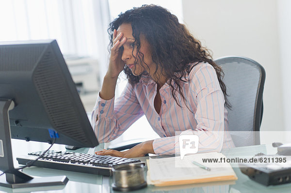 Frustrated Hispanic businesswoman using computer at desk