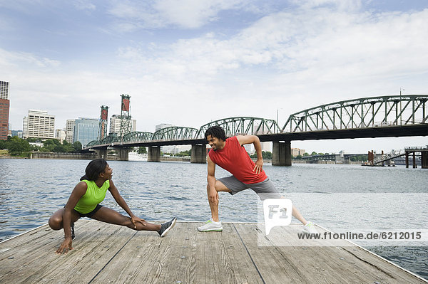 Couple stretching on urban boardwalk along river