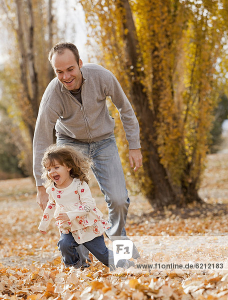 Caucasian father and daughter playing in autumn leaves