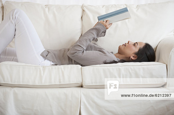 Hispanic woman reading book on sofa