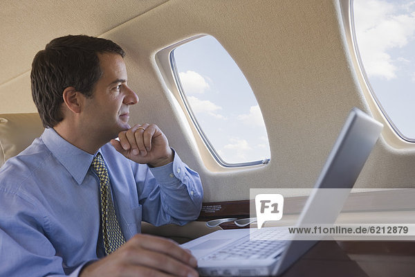 Hispanic businessman with laptop looking out airplane window