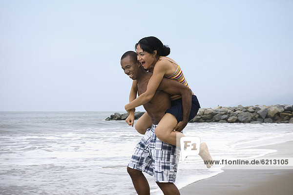 African man giving girlfriend piggy back ride at beach