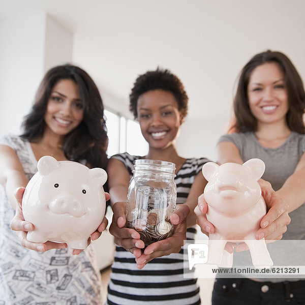 Friends holding out glass jar and piggy banks