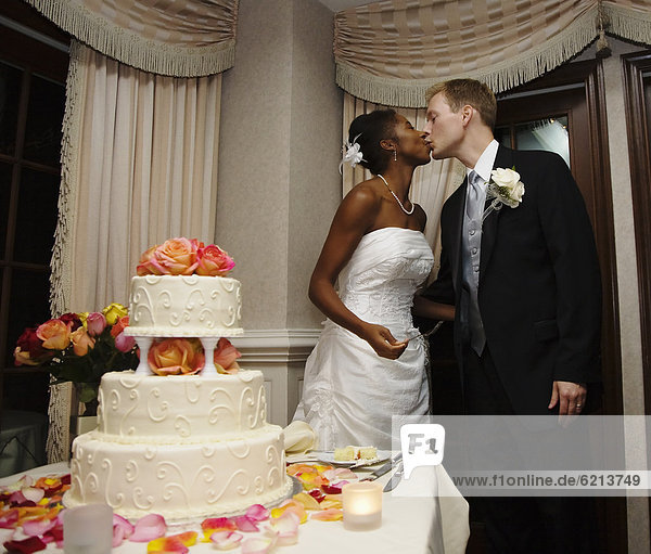Bride and groom kissing next to wedding cake