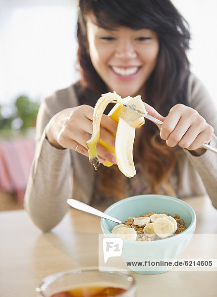 Pacific Islander woman putting bananas on cereal