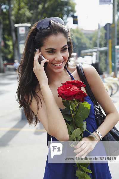 Brazilian woman holding red roses and talking on cell phone