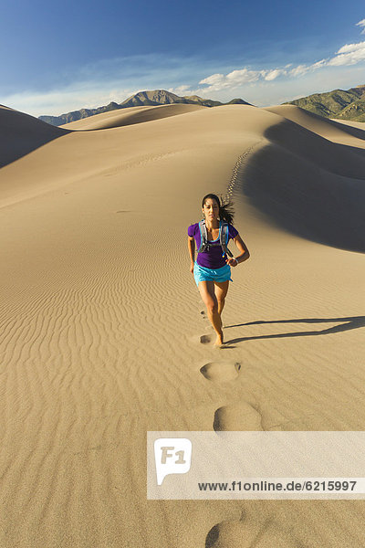 Hispanic woman running on sand dune