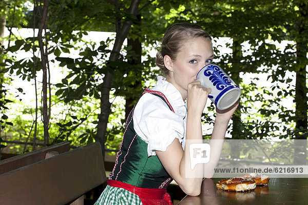 Junge Frau im Dirndl sitzt biertrinkend im Biergarten  bei Pettstatt  Oberfranken  Bayern  Deutschland  Europa