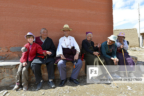 Tibetischer Buddhismus  Pilgergruppe tibetischer Senioren sitzen zusammen mit westlichem Kind an der Klostermauer  Kloster Labrang  Xiahe  Gansu  ehemals Amdo  Tibet  China  Asien