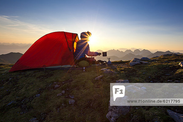 Junge Frau bei Sonnenaufgang vor rotem Zelt  Roter Kogel  Sellrainer Berge  Tirol  Österreich  Europa