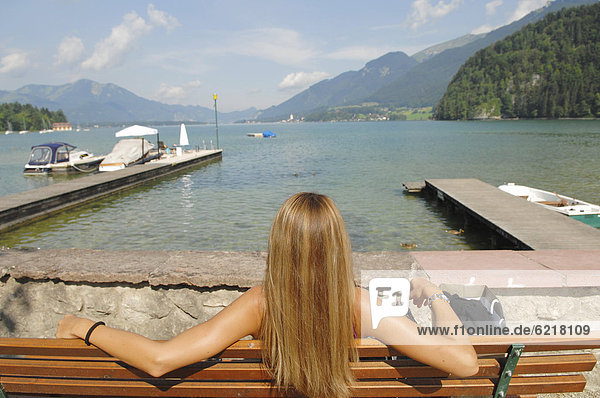 Eine Frau sitzt an einem See und sonnt sich  Wolfgangsee  Salzburg  Österreich  Europa