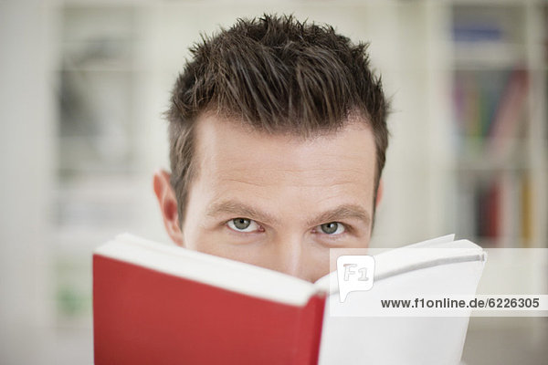 Portrait of a man holding a book in front of his face