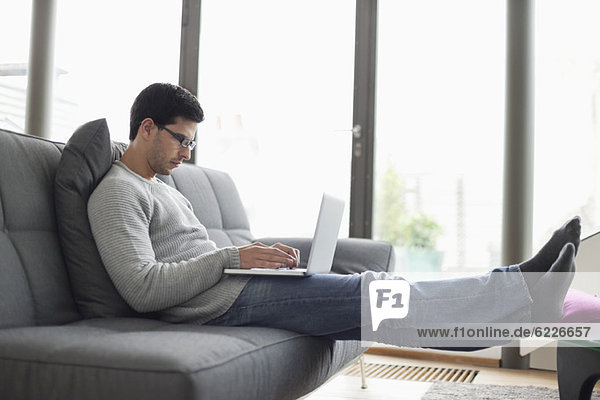 Mann mit einem Laptop auf einer Couch