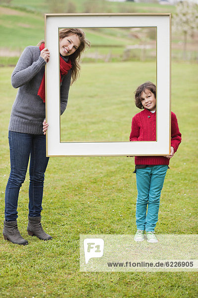 Frau und ihr Sohn stehen mit einem Rahmen in einem Park
