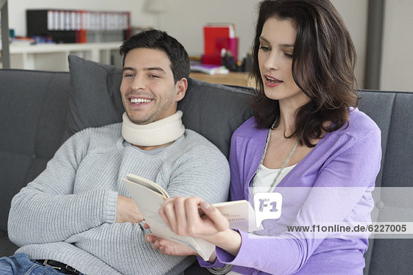 Woman reading a book for her husband suffering from neckache