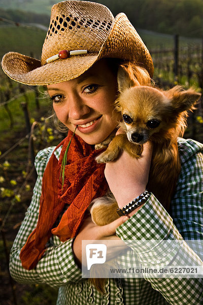 Lächelnde junge Frau mit Hut hält einen Hund  Portrait