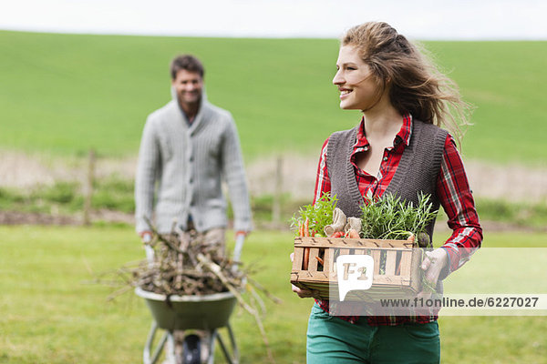 Frau hält einen Korb mit Gemüse und ihr Mann sammelt Brennholz.